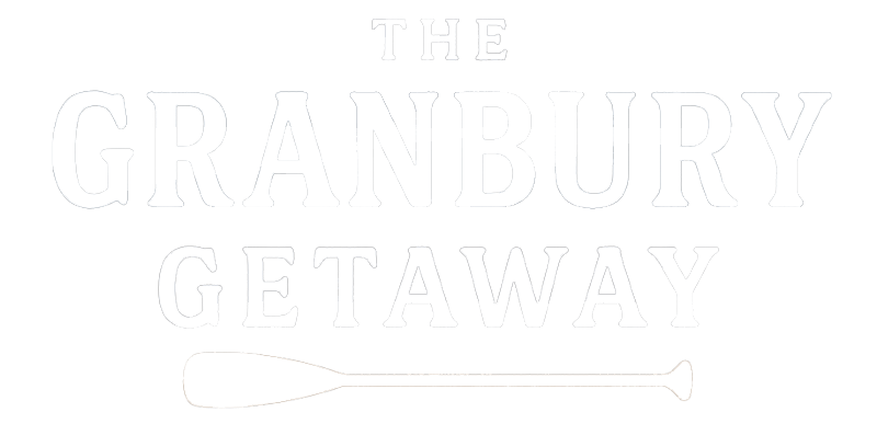 Rustic logo for The Granbury Getaway vacation rental featuring a navy blue house icon, bold serif text, and a brown canoe paddle beneath the name on a textured off-white background.